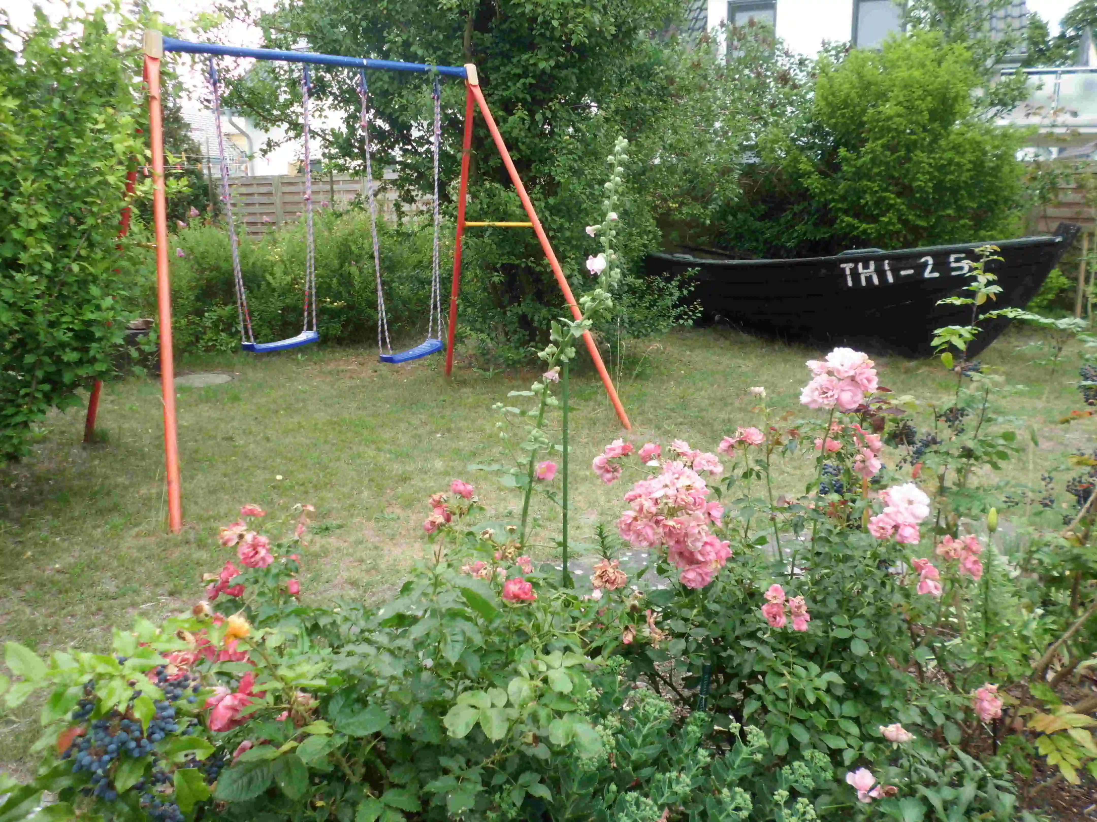 Ein Bild vom Garten von der Ferienwohnung Terrasse aus gesehen mit Schaukel und altem Fischerboot.